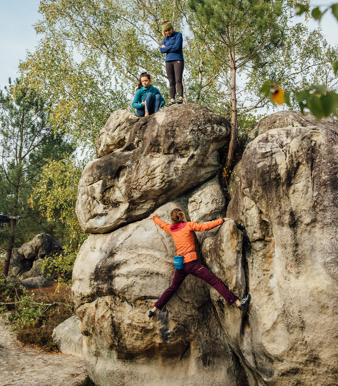 Woman  in red and orange bouldering with two friends helping her navigate the climb